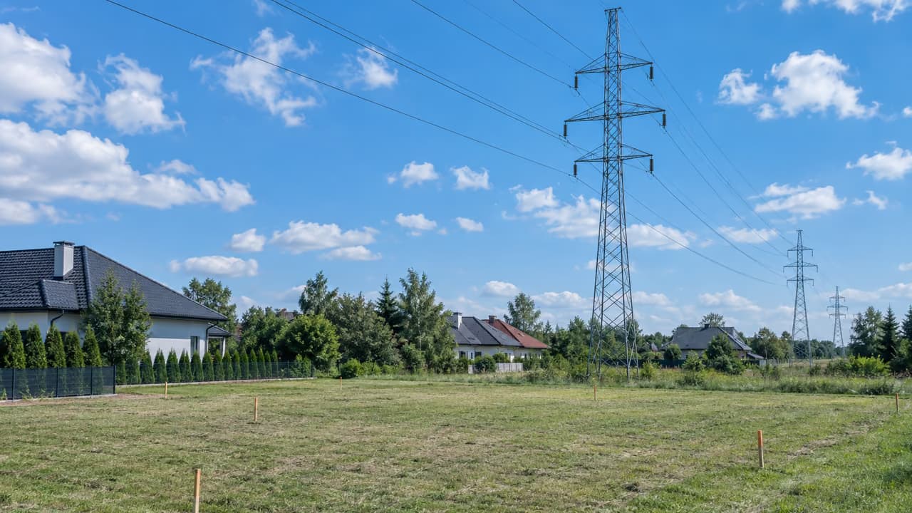 Linia wysokiego napięcia i słupy nad wydzieloną działką budowlaną