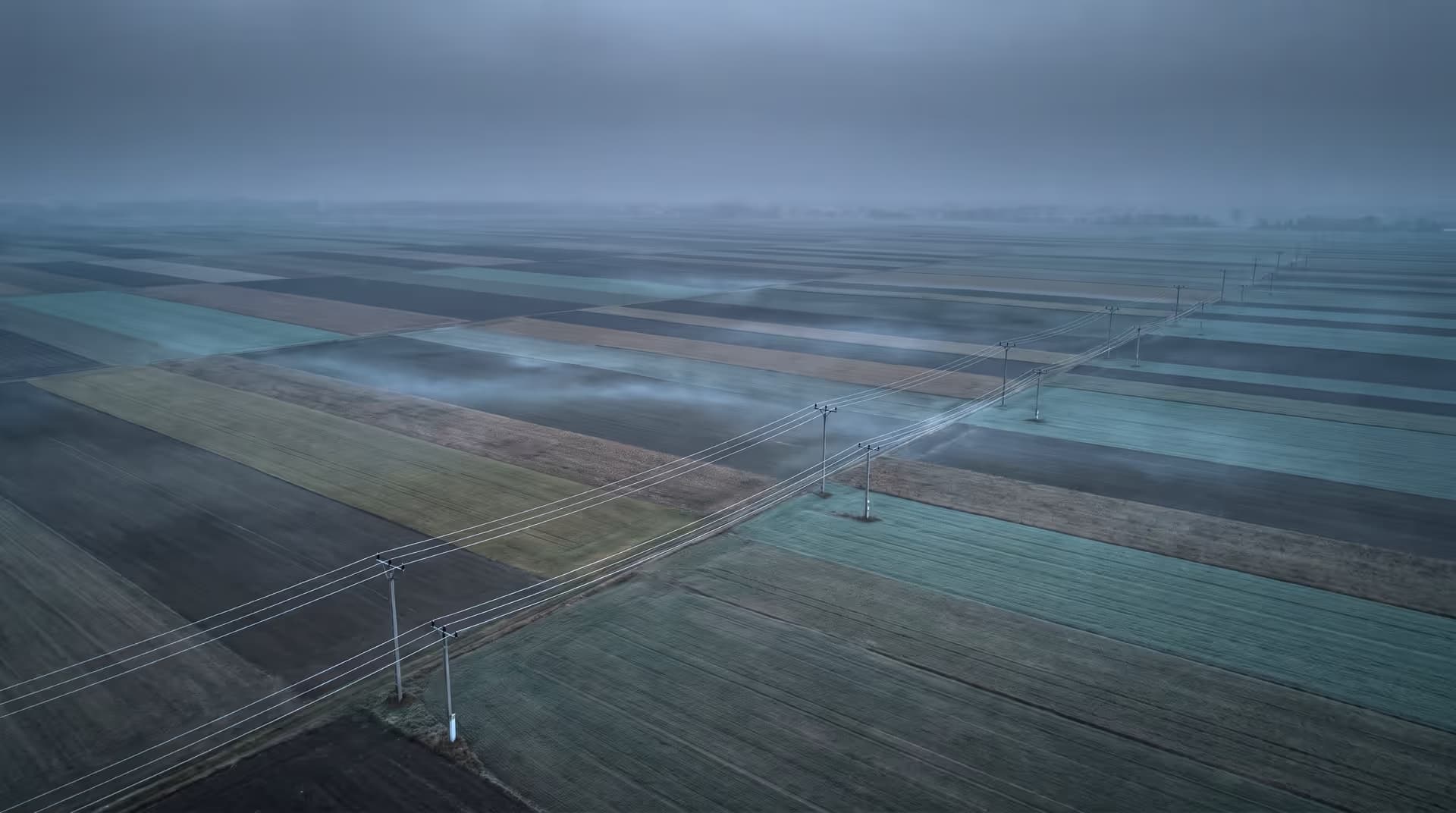 Widok z lotu ptaka na pola uprawne z linią energetyczną przecinającą je po skosie