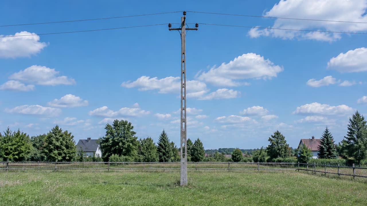 Słup energetyczny pośrodku ogrodzonej, prywatnej łąki