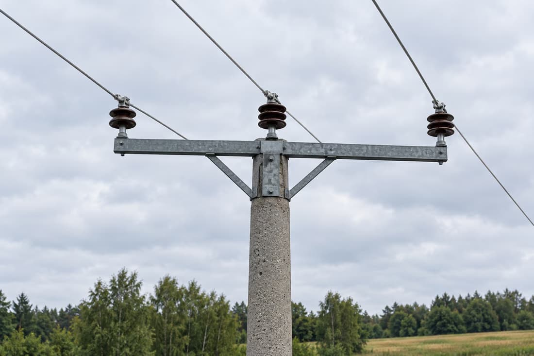 Szczyt betonowego słupa na tle zachmurzonego nieba: stalowa poprzeczka i trzy osobne przewody, każdy na własnym izolatorze