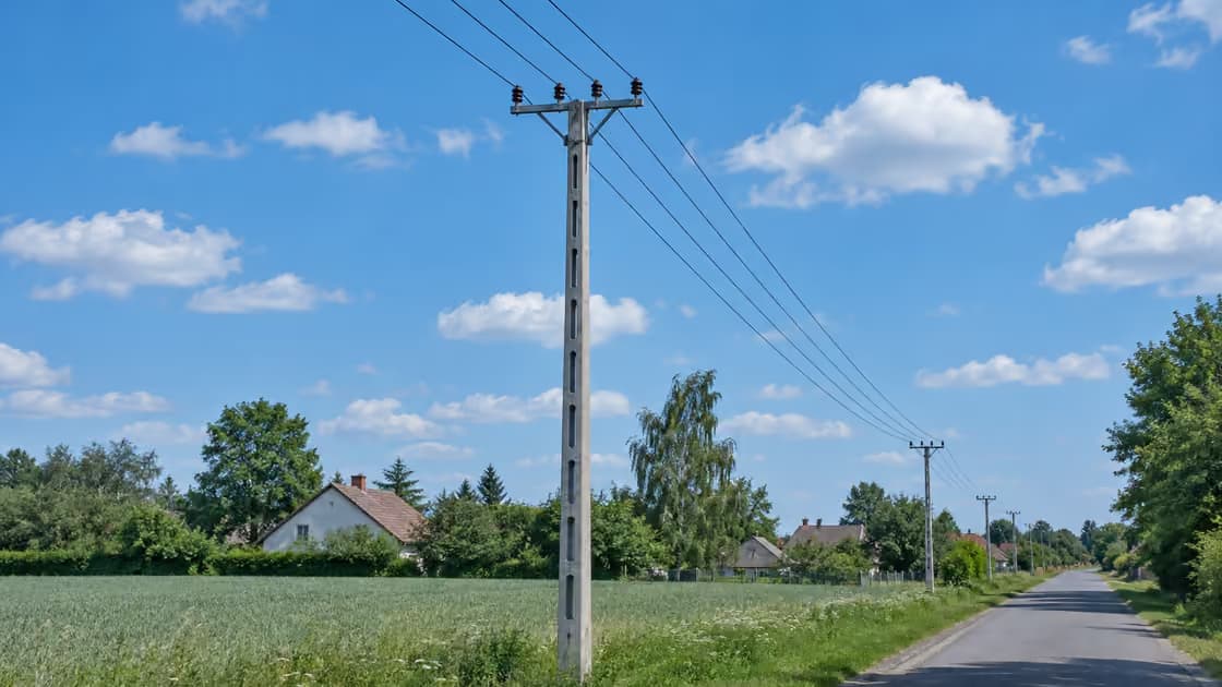 Słup betonowy niskiego napięcia przy wiejskiej drodze, cztery przewody na poprzeczniku